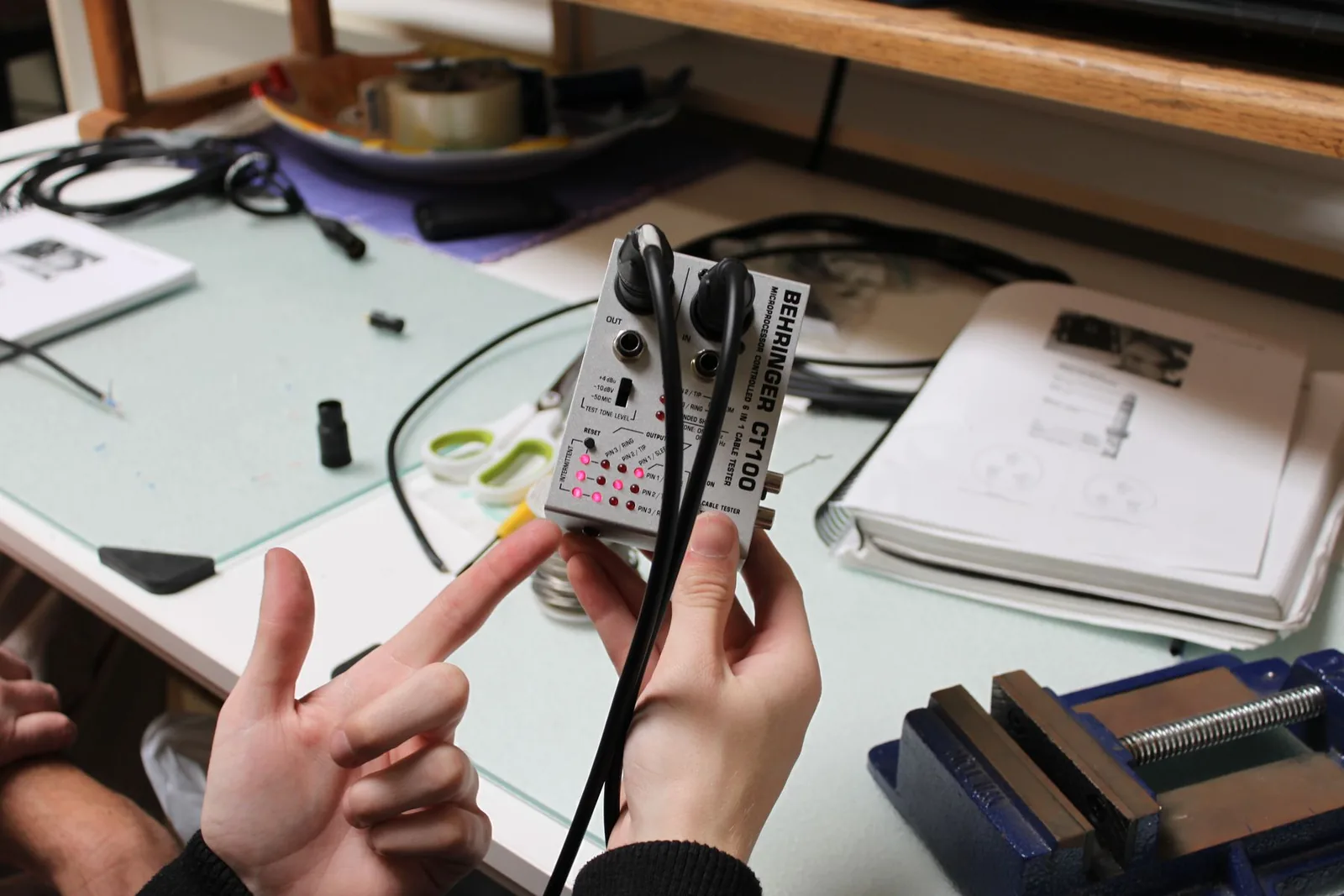 Photo of a Behringer CT100 cable tester with an XLR cable plugged into both ends, displaying continuity indicator lights for all three pins.
