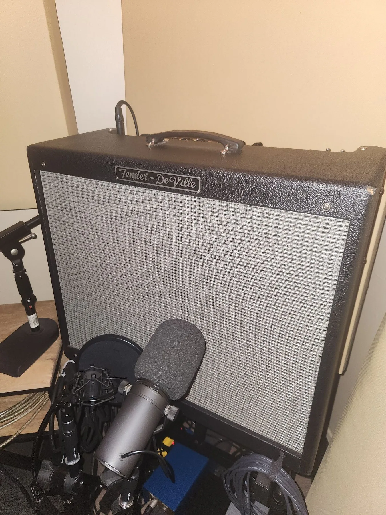 Photo of a dynamic microphone positioned close to the speaker grille of a Fender guitar amplifier.
